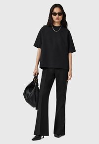 Zwarte oversized t-shirt met korte mouwen, gecombineerd met zwarte flare-broeken. Accessoires zijn onder andere zwarte zonnebril, een zilveren kettinghalsketting en een zwarte tas.