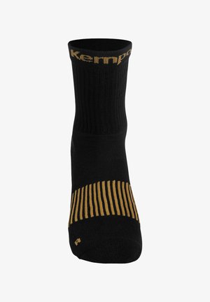 Chaussette noire à texture côtelée avec un accent doré. Présente un logo en haut et des bandes verticales le long du bas pour l'adhérence.