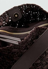 Interno della borsa intrecciata di colore marrone scuro con zip dorata, foderata in tessuto nero e con una tracolla in pelle con chiusura a bottone a pressione.