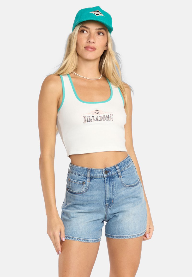 White ribbed crop top with aqua trim, featuring "BILLABONG" text. Light blue denim shorts with a high waist and frayed edges. Aqua baseball cap.