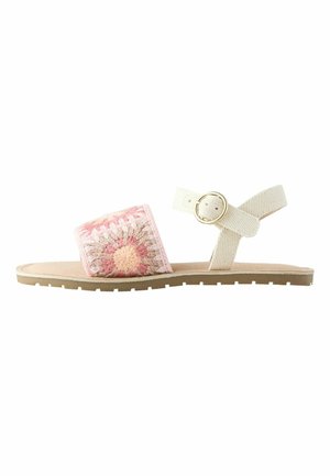Flache Sandale mit einem rosa und beige gehäkelten Vorderriemen und einem beigen Knöchelriemen mit goldener Schnalle.