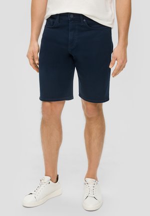 Shorts en denim bleu marine avec une coupe droite, cinq poches et passants de ceinture. Associés à des baskets blanches avec des accents noirs.