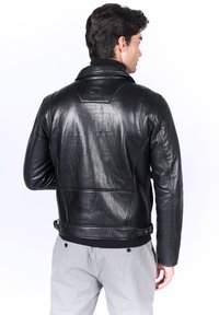 Chaqueta de moto de cuero negro con un diseño acolchado en el cuello, broches laterales y un corte ajustado con una cinturilla acanalada.