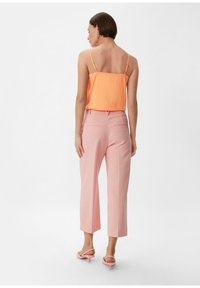 Jasnoróżowy satynowy top na ramiączkach z cienkimi paskami, zestawiony z jasnoróżowymi, krótkimi spodniami o dopasowanym kroju, wyposażonymi w tylne kieszenie i luźnym fasonie, noszony z różowymi sandałami na obcasie.