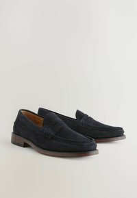 Mocasines de ante azul marino con un acabado suave, detalles cosidos y suelos de cuero. El diseño incluye un tacón plano y una silueta clásica.
