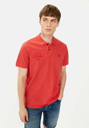 Rotes Poloshirt mit Kragen, Knopfleiste mit drei Knöpfen und kurzen Ärmeln. Es verfügt über gestickten Text auf der Brust und ein Logo an der Seite.