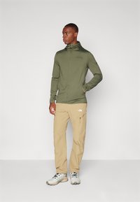 Olive green zip-up jacket with a fitted design; light khaki cargo pants featuring side pockets; gray and white athletic shoes.