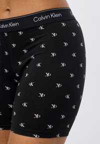 Μαύρα αντρικά εσώρουχα boxer με διάσπαρτα λευκά λογότυπα Calvin Klein. Μαλακό υλικό με ελαστική μέση που φέρει το όνομα της μάρκας.