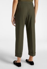 Pantaloni impeccabili verde oliva con una vestibilità rilassata, orli a fondo risvoltato e una texture liscia, abbinati a scarpe basse nere.