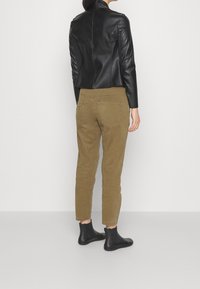 Veste courte en cuir noir associée à un pantalon en velours côtelé beige. Le pantalon comporte des poches plaquées et une coupe fuselée. Bottines noires visibles.