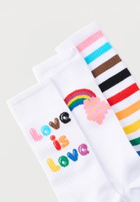 Τρία λευκά καλτσάκια με πολύχρωμα σχέδια: κείμενο "Η αγάπη είναι αγάπη", ουράνιο τόξο με ροζ σύννεφο και οριζόντιες ρίγες ουράνιου τόξου.