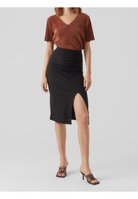 Haut marron à col en V côtelé associé à une jupe midi noire ajustée avec fronces sur le côté et une fente haute sur la cuisse. Sandales à talons bruns à lanières.