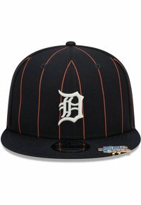 Schwarze Baseballmütze mit vertikalen orangen Streifen, die ein auffälliges weißes gesticktes "D"-Logo und ein flaches Schild aufweist. Mit einem Logosticker.