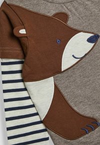 Brunbjørn grafisk design på en sandfarvet skjorte med stribede beige og navy ærmer. Funktioner inkluderer detaljeret broderi og blødt stoftekstur.