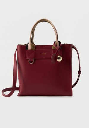 Δερμάτινη τσάντα Furla σε μπορντό με μπεζ υφασμάτινες χειρολαβές, χρυσό λογότυπο, μικρό χρυσό γούρι και αφαιρούμενο ιμάντα ώμου σε λευκό φόντο.