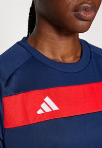 Marineblauw sportshirt met een opvallende rode horizontale band en wit logo. Heeft een ronde halslijn en een gladde textuur.