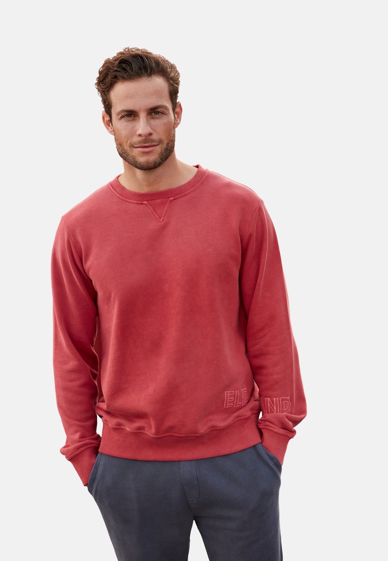 Rode sweatshirt met een ronde hals en ribgebreide manchetten. Voorzien van een geborduurd logo detail aan de onderrand en een relaxte pasvorm. Gepaard met grijze broek.
