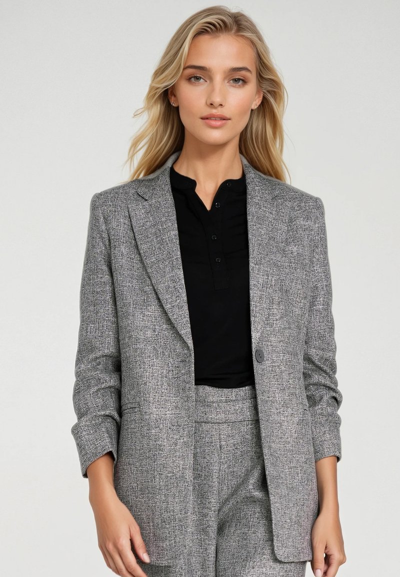 Szary, fakturowany żakiet o dopasowanym kroju, z pojedynczym zapięciem na guzik i wyłóżnymi klapami. Noszony na czarnym topie z kołnierzykiem.