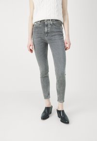 Los jeans skinny de mezclilla gris cuentan con una cintura alta, cinco bolsillos y un desgastado sutil. Se combinan con zuecos negros de tacón para un estilo moderno.