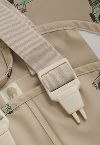 Matériau beige avec une sangle en tissu texturé et une boucle en plastique. Comprend des designs de véhicules imprimés et un petit logo d'éléphant.
