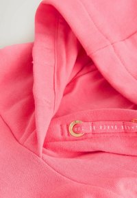 Vaaleanpunainen huppari pehmeällä pinnalla, jossa on huppu, kultaiset yksityiskohdat ja kiristysnauha, jossa on brändilogo.