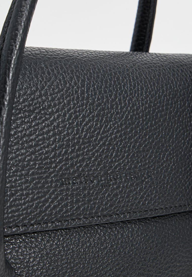 Sac à main en cuir noir avec une surface texturée, une forme structurée et un logo en relief. Deux poignées pour le transport.