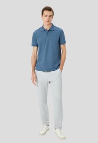 Polo blu con maniche corte, colletto classico; abbinato a pantaloni grigi chiari e sneakers bianche. Tessuto liscio, design semplice.