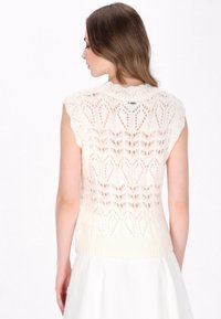 Ärmelloses Stricktop in Creme mit einem Spitzenmuster und welligen Details an den Schultern, mit einem enganliegenden Rippabschluss.