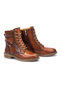 Brown leather ankle boots with a lace-up front, side zipper, and rubber sole. Features a smooth texture and decorative strap with a ring.