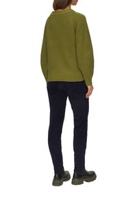 Olivgrüner, gestrickter Pullover mit lockerem Schnitt, gerippten Bündchen und Saum, kombiniert mit marineblauen Hosen und robusten schwarzen Stiefeln.