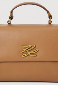 Borsa in pelle marrone con una forma strutturata. Presenta un manico superiore, hardware in tonalità oro e un logo in rilievo sul davanti. Tessuto liscio.