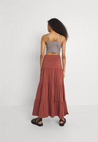 Crop top gris avec des fines bretelles, associé à une jupe maxi tiered couleur rouille en tissu doux. Comprend une taille élastique et une coupe décontractée.