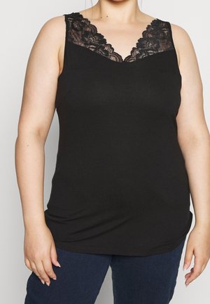 Vrouw draagt een zwart mouwloos topje met bloemenkantdetail bij de halslijn en donkerblauwe spijkerbroek.