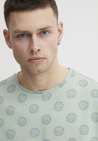 Lys grønn t-skjorte med et sirkulært grafisk mønster i marineblått. Rund hals-design med en myk tekstur og korte ermer.