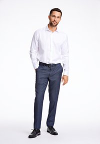 Camicia bianca con bottoni, pantaloni eleganti navy, scarpe eleganti nere. La camicia è semplice e i pantaloni hanno una texture sottile e una vestibilità slim.