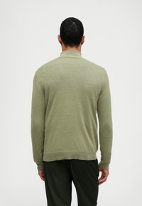 Grön stickad tröja med ribbad krage och mudd. Har en avslappnad passform och en jämn textur, visas från baksidan.