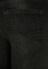 Černé denimové džíny s zadní kapsou a zakřiveným švem, hladkou texturou a jemným leskem.