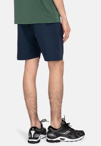 Navy blue shorts with a smooth texture, paired with black and white athletic shoes featuring a mesh design and distinct sole.