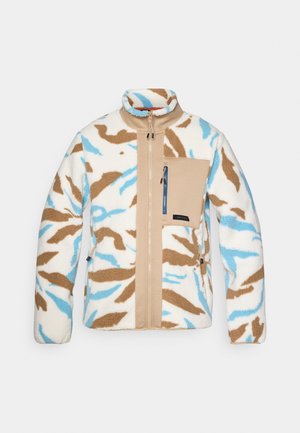 Chaleco de forro polar en blanco, beige y patrón de camuflaje azul. Cuenta con un cierre frontal, cuello alto y un bolsillo en el pecho beige con cierre de cremallera.