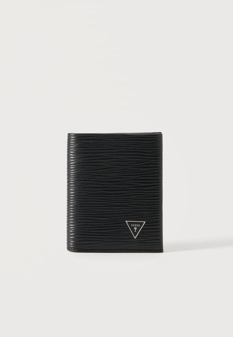Portefeuille en cuir noir texturé avec un petit logo Guess argenté en forme de triangle dans le coin inférieur droit, debout sur une surface blanche.