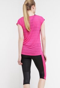 Åtsittande, kortärmad rosa sporttop med en texturerad mönster, i kombination med capril leggings i svart och rosa färgblock. Slät tyg, atletisk design.