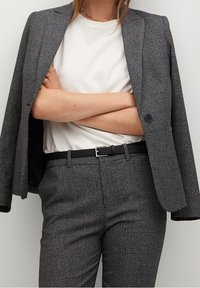Szary, w kratkę żakiet połączony z białym t-shirtem, spodniami z paskiem oraz cienkim, złotym naszyjnikiem; materiał ma gładką teksturę i jest starannie skrojony.