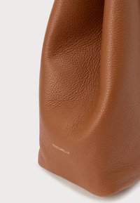 Brown textured leather handbag with soft folds, displaying gold "Coccinelle" logo near the bottom edge on a white background.