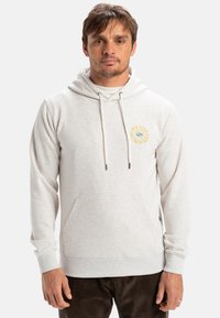 Lys grå sweatshirt med hætte, der har en frontlomme, snore og et rundt logo på brystet. Blød tekstur og afslappet pasform.