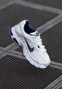Białe i granatowe buty biegowe Nike z siateczkową cholewką, gumową podeszwą i wyściełanym kołnierzem. Posiadają wyraźny slogan oraz teksturowane elementy designu.