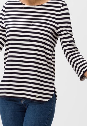 Bluzka w paski w kolorze granatowym i białym z okrągłym dekoltem, długimi rękawami, kieszenią na piersi i bocznymi rozcięciami, wykonana z miękkiego materiału.