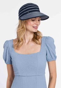 Jūrų įkvėptas margas kepuraitė pagaminta iš audinio, su plačiu kraštu ir minkšta tekstūra. Modelis vilki šviesiai mėlyną tekstūruotą suknelę su pūstomis rankovėmis.