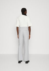 Bílý top s krátkým rukávem v kombinaci s světle šedými rozšířenými kalhotami. Kalhoty mají hladký povrch a dvě zadní kapsy. Černé kotníkové boty dotvářejí vzhled.