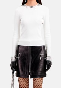 Biały sweter z długim rękawem i ozdobnym dekoltem, zestawiony z czarną skórzaną spódnicą z zamkiem błyskawicznym i rajstopami w siateczkę.