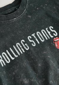 Mustan hupparin teksturoitu pinta, jossa on "ROLLING STONES" valkoisella kirjoitettuna ja punainen kielilogo. Ribattu kaulus.